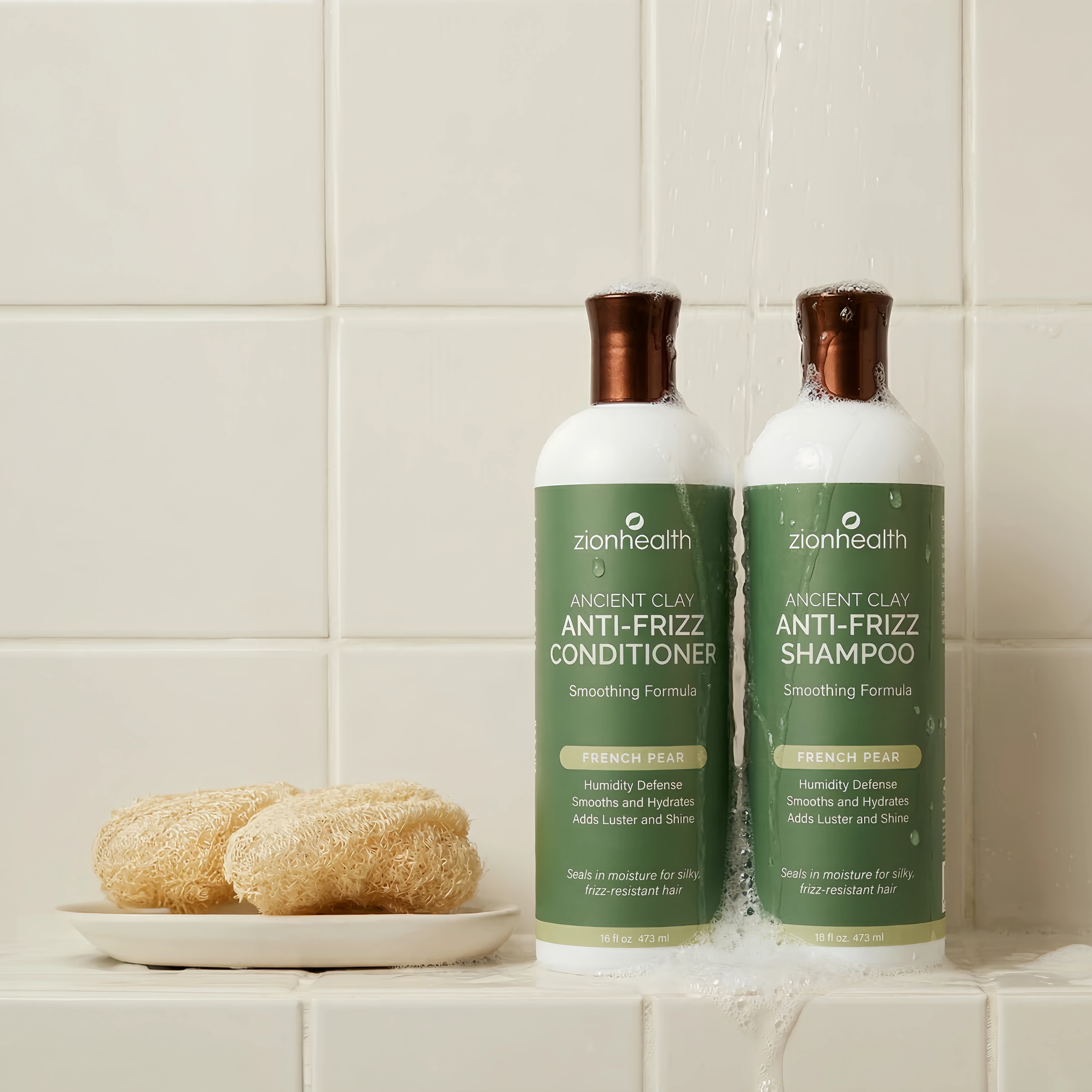 A white bottle of Zionhealth Ancient Clay Anti-Frizz Conditioner next to two natural loofah sponges.