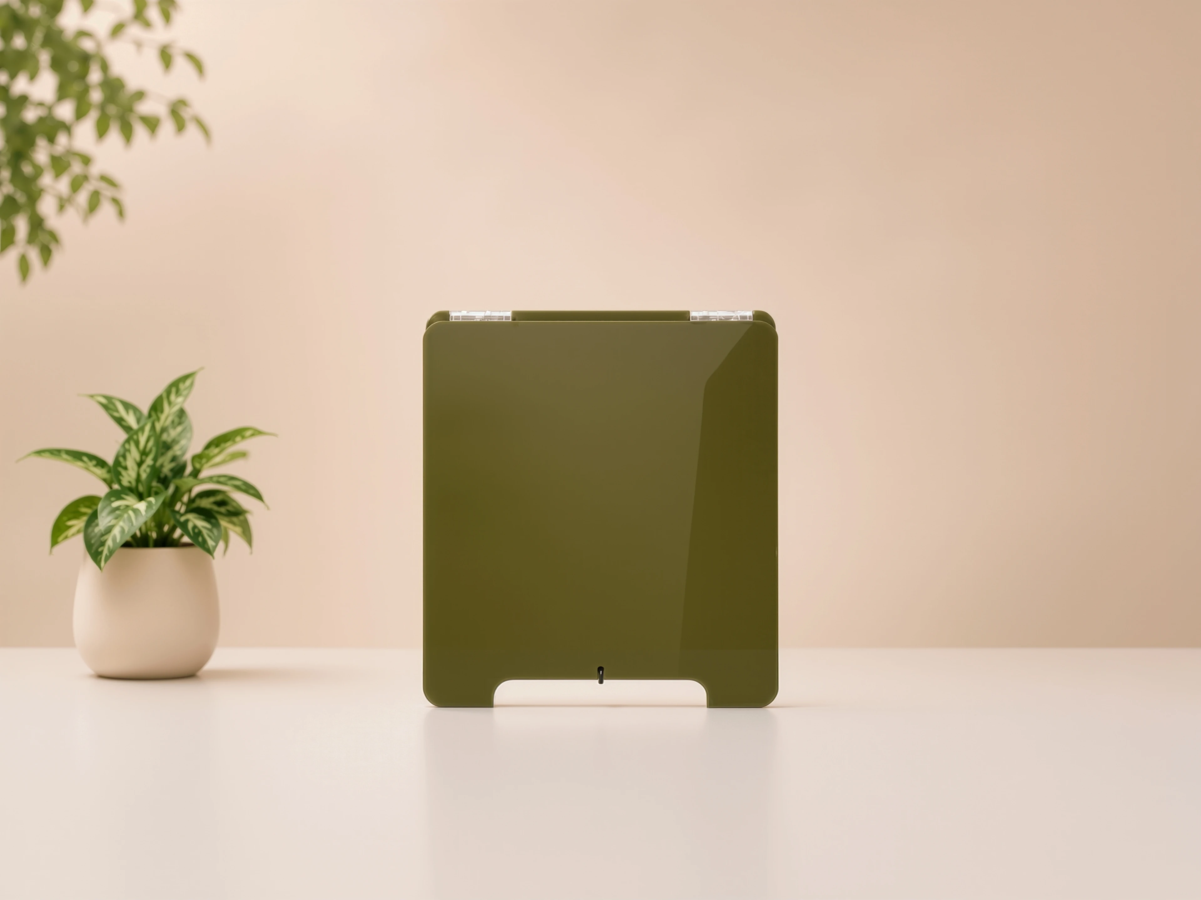 A blank olive green acrylic MUUJEE sign stand on a table beside a potted plant.