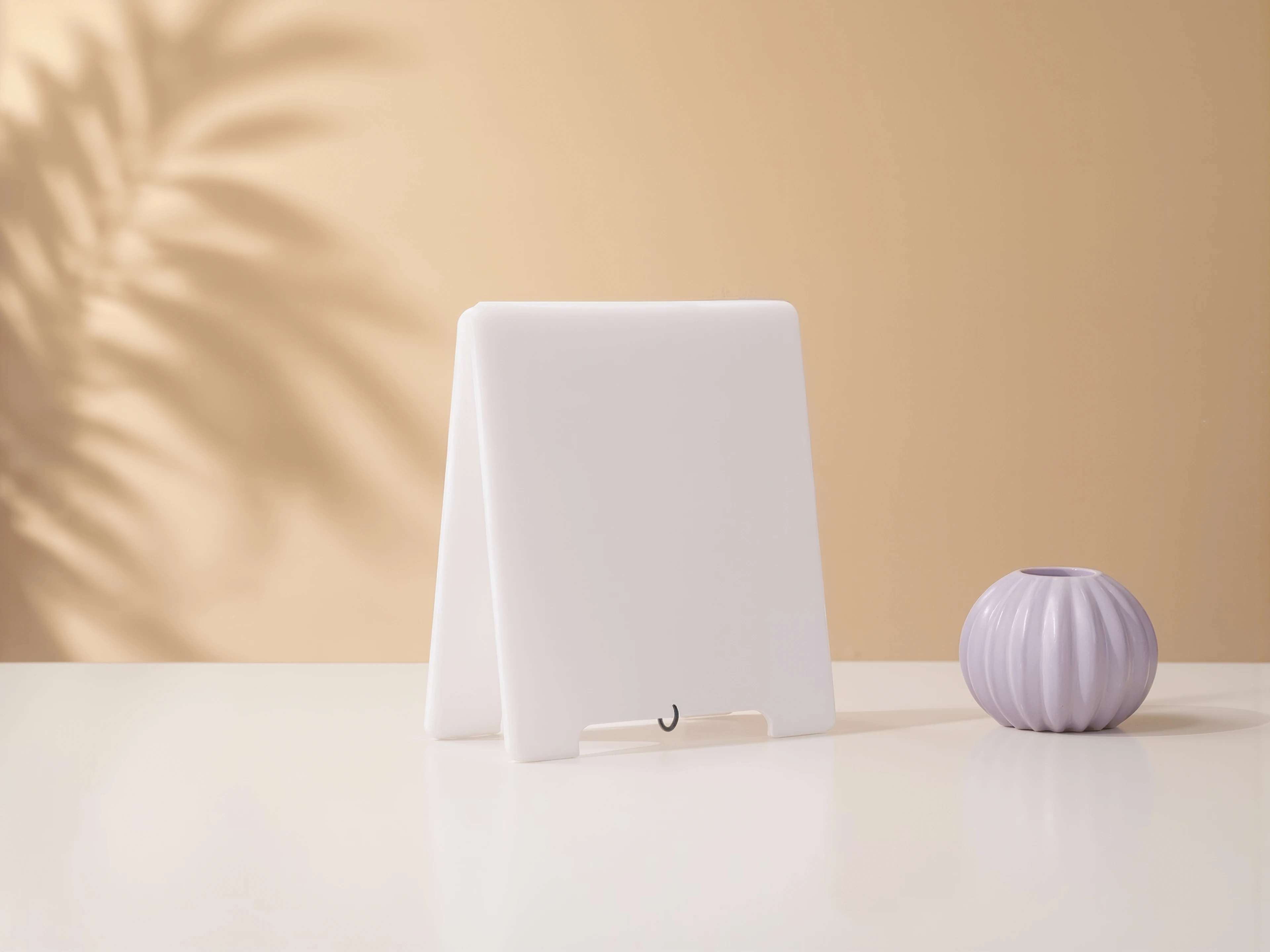 A blank white acrylic MUUJEE sign stand angled on a table beside a small vase.