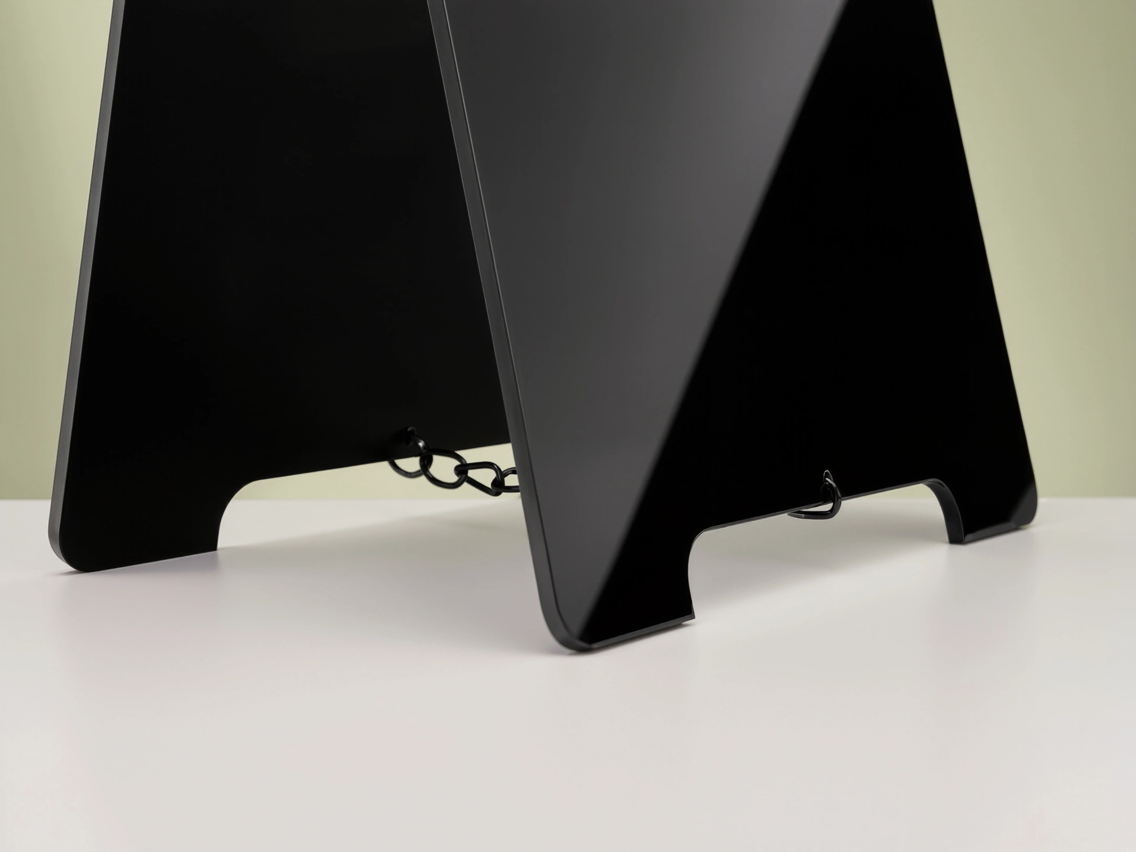 Close-up of a black acrylic MUUJEE A-frame sign stand with a chain detail connecting the two panels.