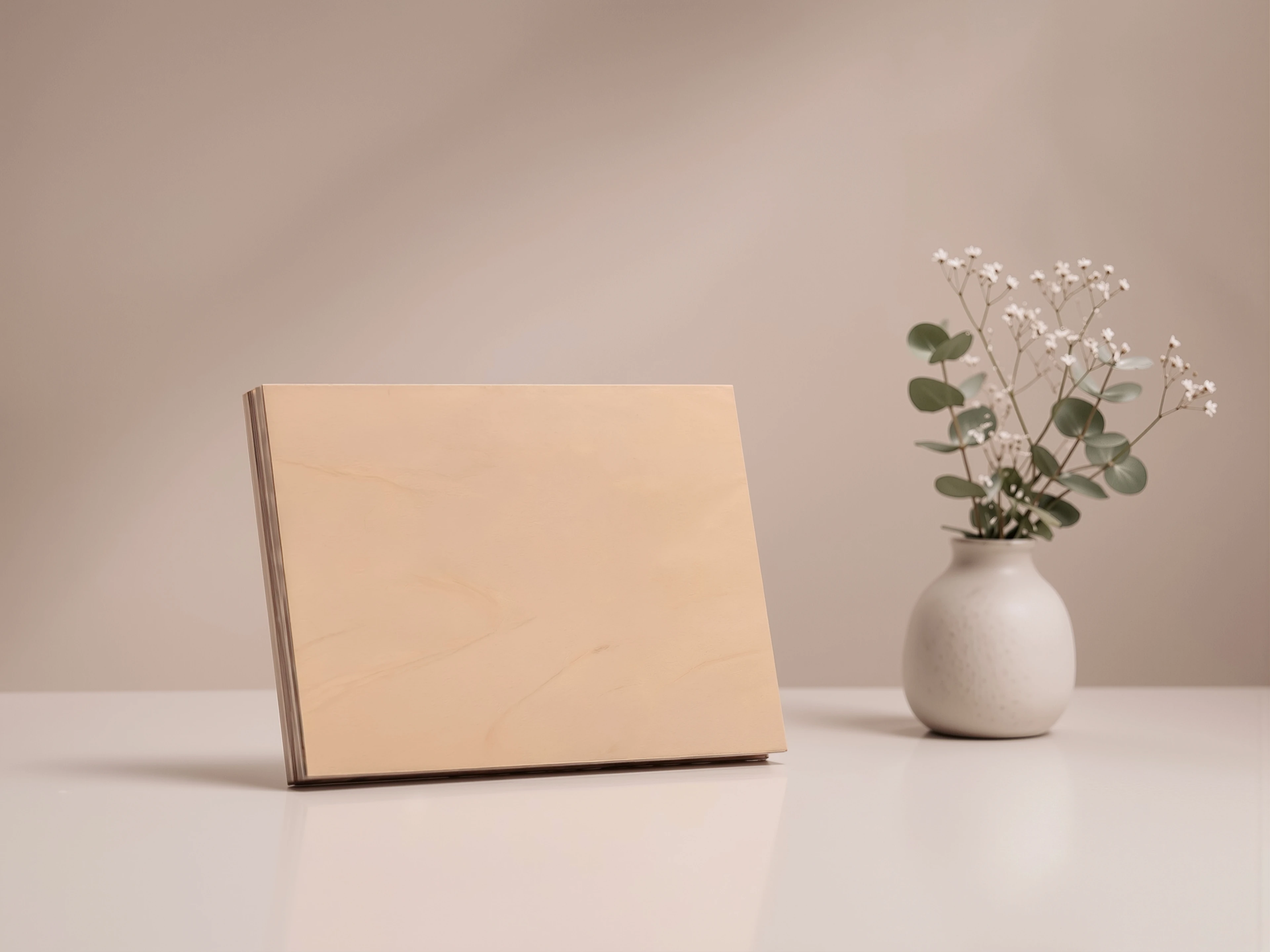 A blank light maple MUUJEE album cover resting on a table beside a vase of flowers.
