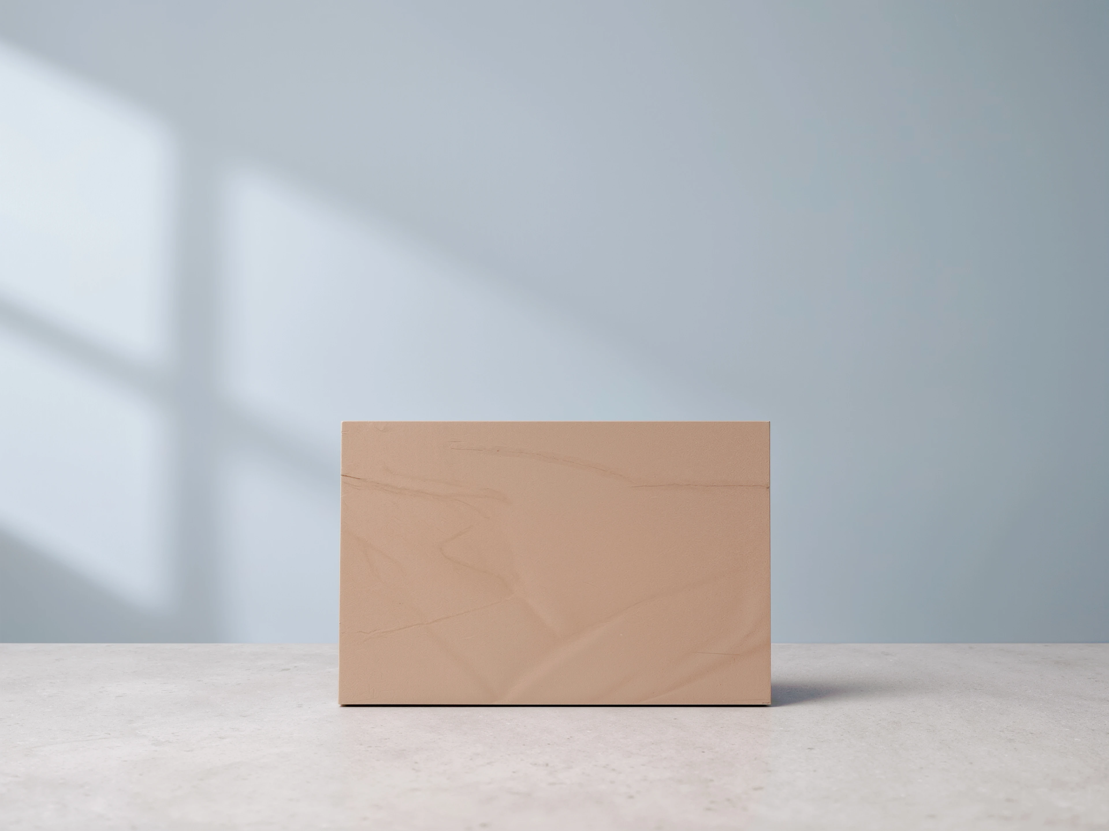A blank tan MUUJEE album cover photographed against a soft blue-grey backdrop.