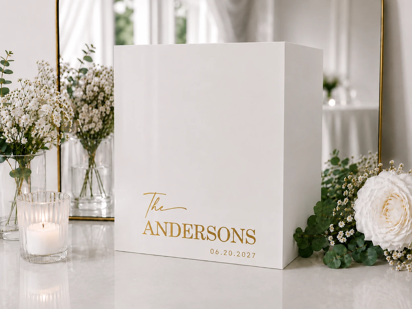 A white MUUJEE keepsake box personalized with 'The Andersons' in gold foil script, styled with candles and flowers.