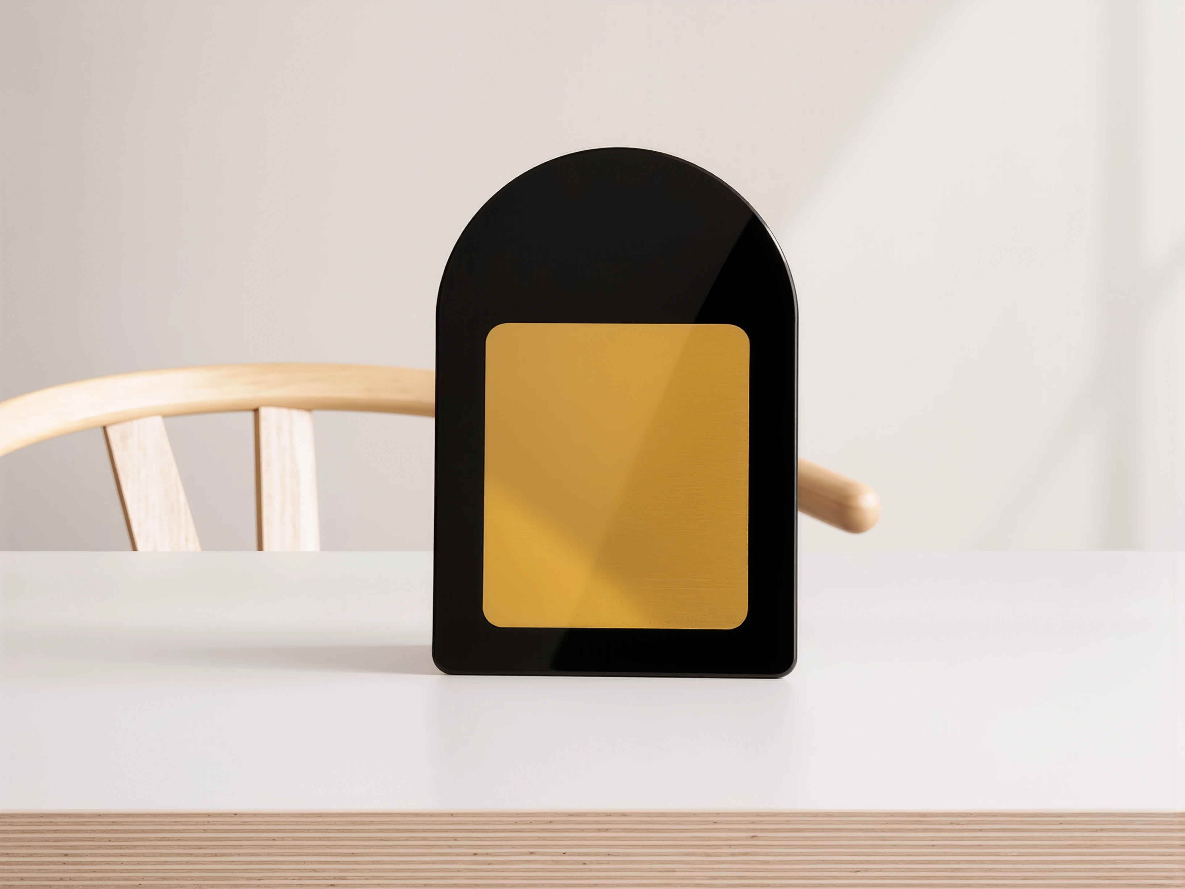 A black arched MUUJEE sign with a brushed gold metal plate insert, styled on a desk with a wooden chair.