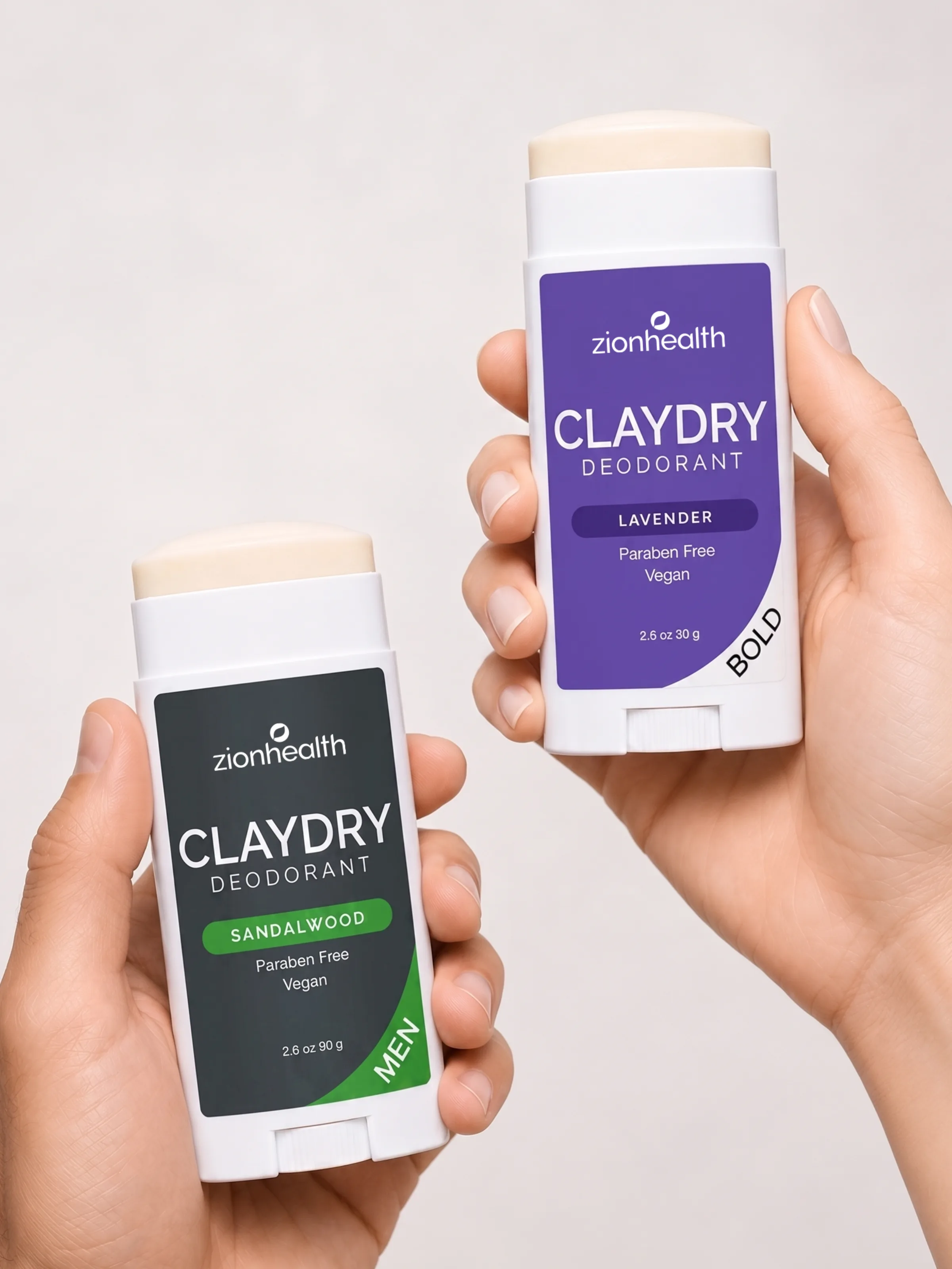 Two hands holding Zion Health Claydry Deodorant sticks in Sandalwood Men and Lavender Bold scents.