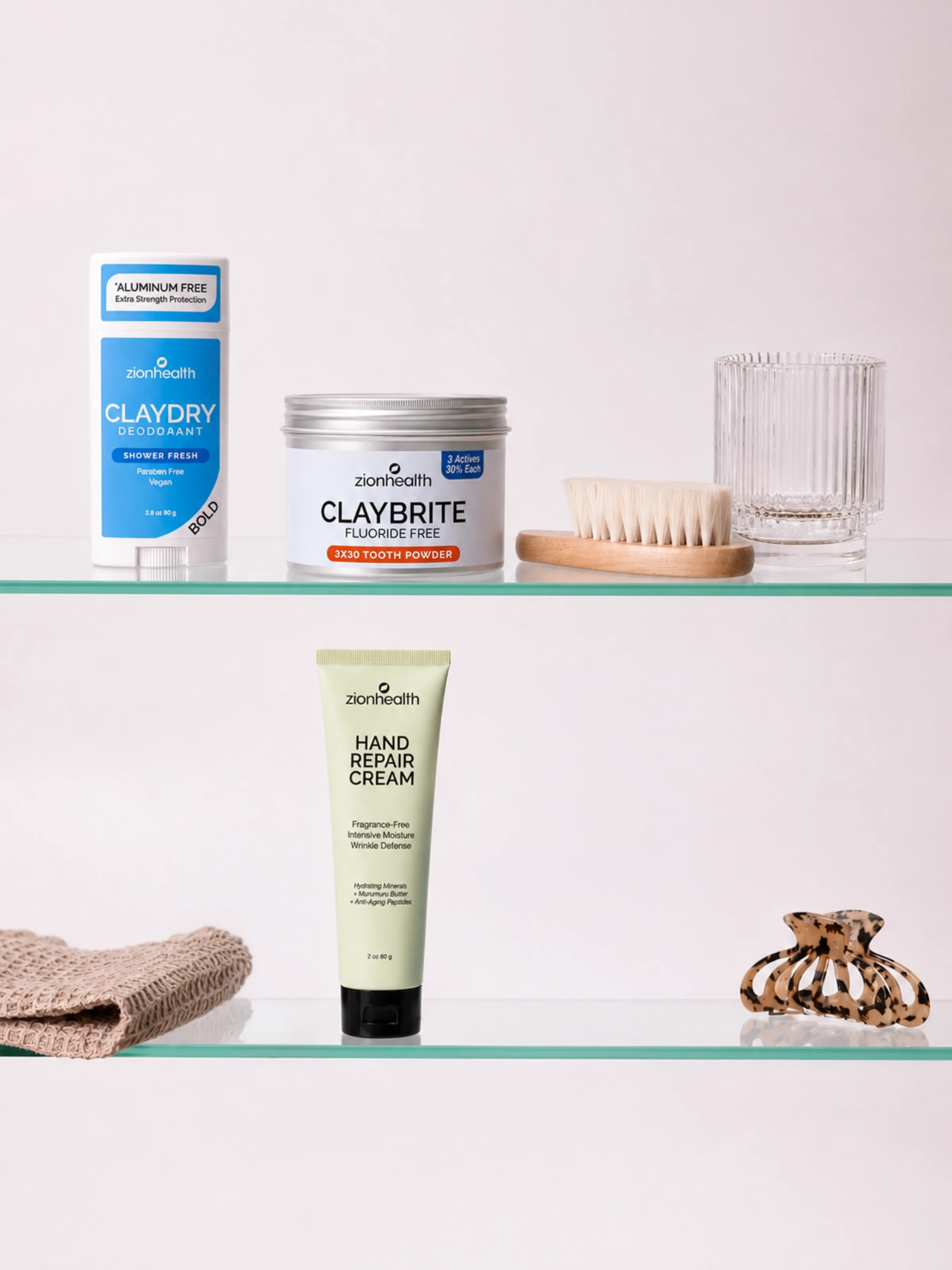 A bathroom shelf styled with Zion Health Claydry Deodorant, Claybrite tooth powder, a bamboo brush, and Hand Repair Cream.