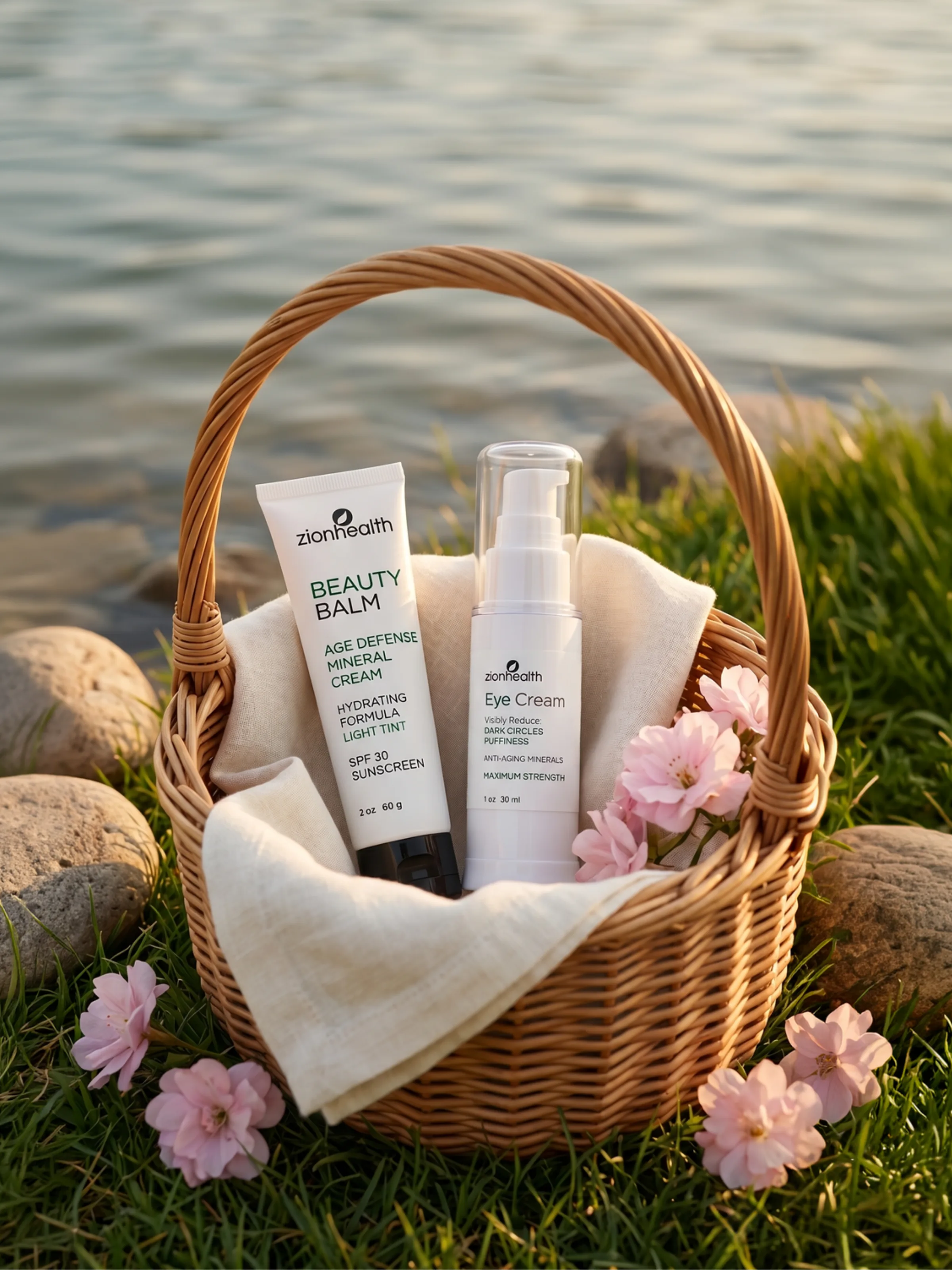 Zion Health Beauty Balm and Eye Cream displayed in a wicker basket beside a lake with pink blossoms.
