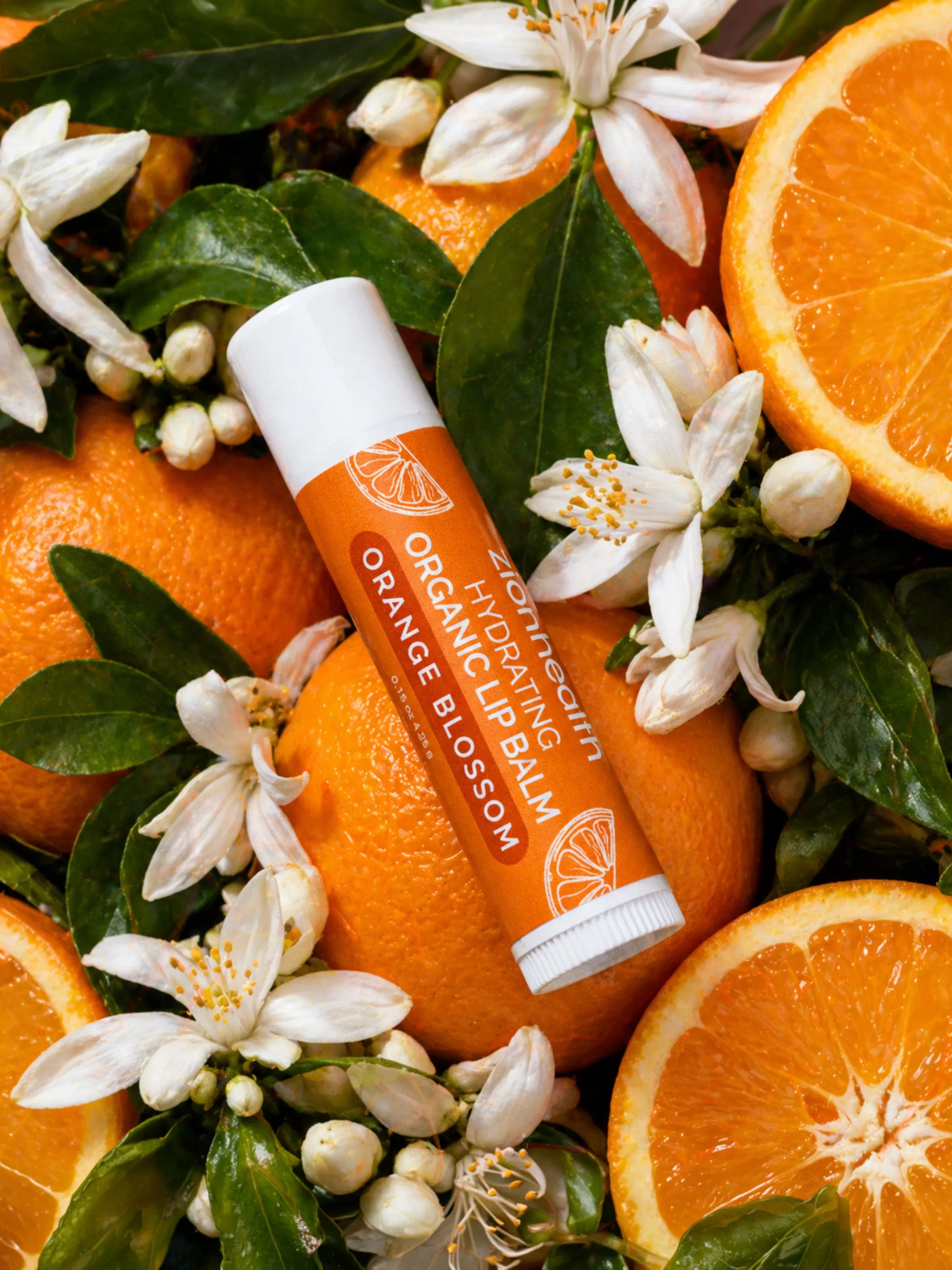 Zion Health Organic Hydrating Lip Balm in Orange Blossom, styled among orange slices and blossoms.
