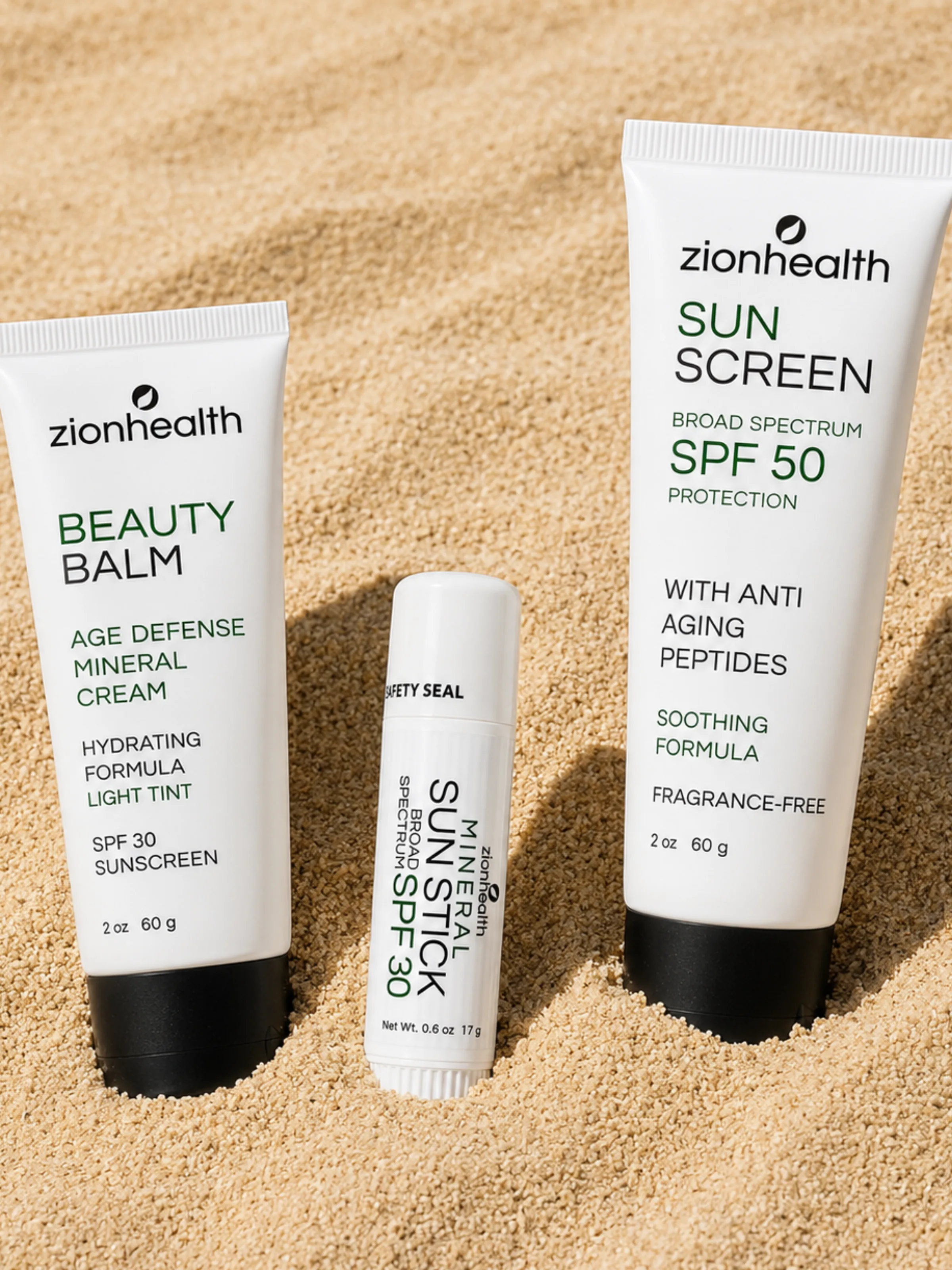 Zion Health Beauty Balm, Mineral Sun Stick SPF 30, and Sunscreen SPF 50 arranged in beach sand.